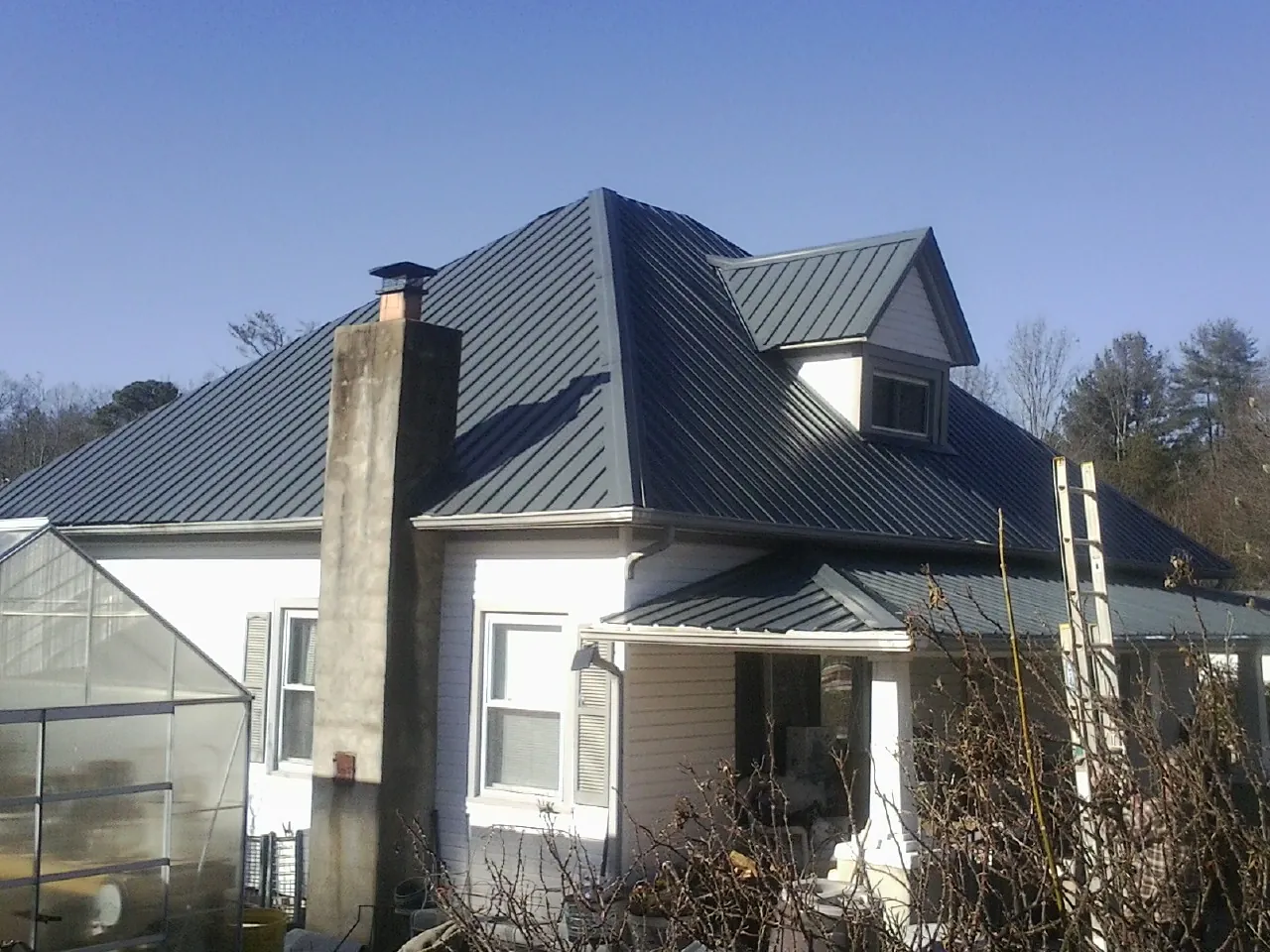 Dark blue standing seam metal roof on a white farmhouse with dormer — Slate & Tile Roof Repair by Roofing Brothers in Big Sky