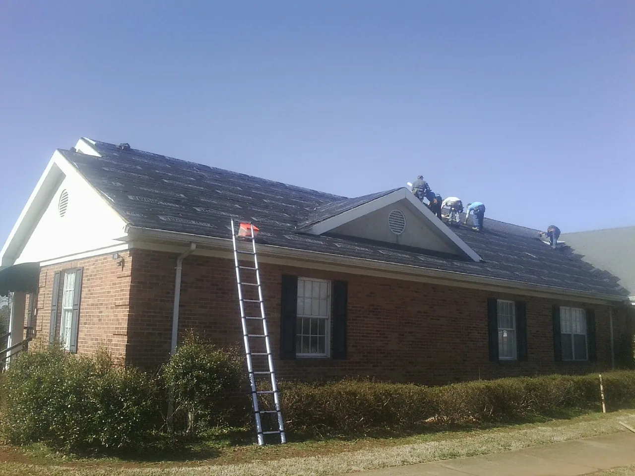 Crew tearing shingles off a brick ranch roof with a ladder set — Metal Roof Repair work by our crew in Big Sky