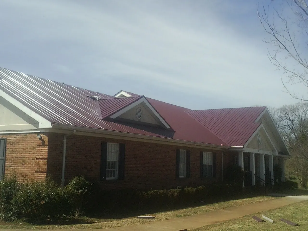 Red metal roof with gabled entries on a long brick building, from a Hail Damage Roof Repair job in Big Sky