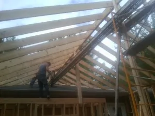 Rafters going up over a new addition with a worker on the wall in Big Sky