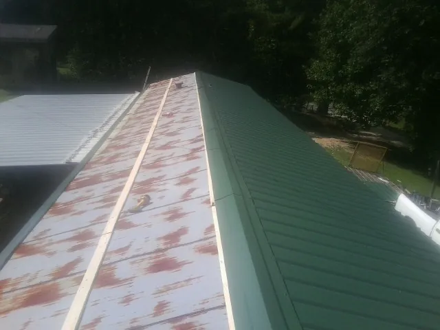 Old rusted panels beside newly installed green metal roofing — Wind Damage Roof Repair by Roofing Brothers in Big Sky