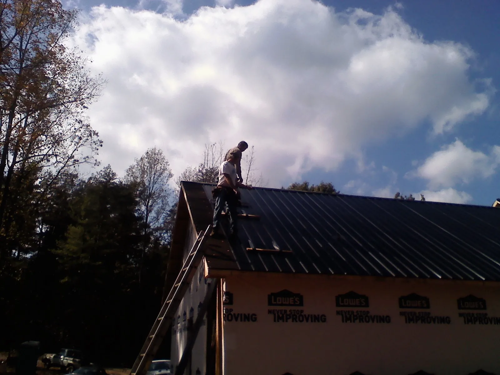 Roofer fastening dark metal panels high against a cloudy sky, from a Roof Inspection job in Big Sky